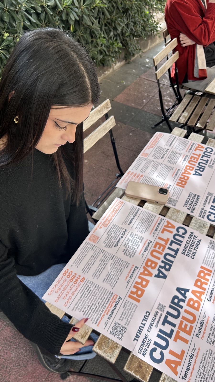 Lectora con el mantel monográfico Cultura al teu barri de Gato News en una terraza de Barcelona